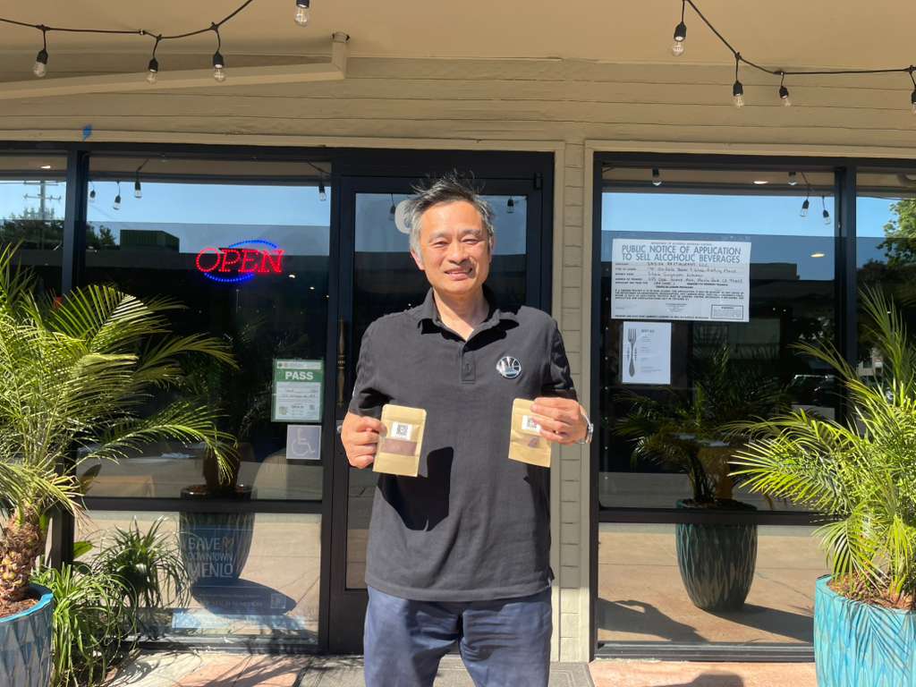 Dennis Lim holding bags of cacao in front of Shiok Singapore Kitchen at 625 Oak Grove Avenue, Menlo Park